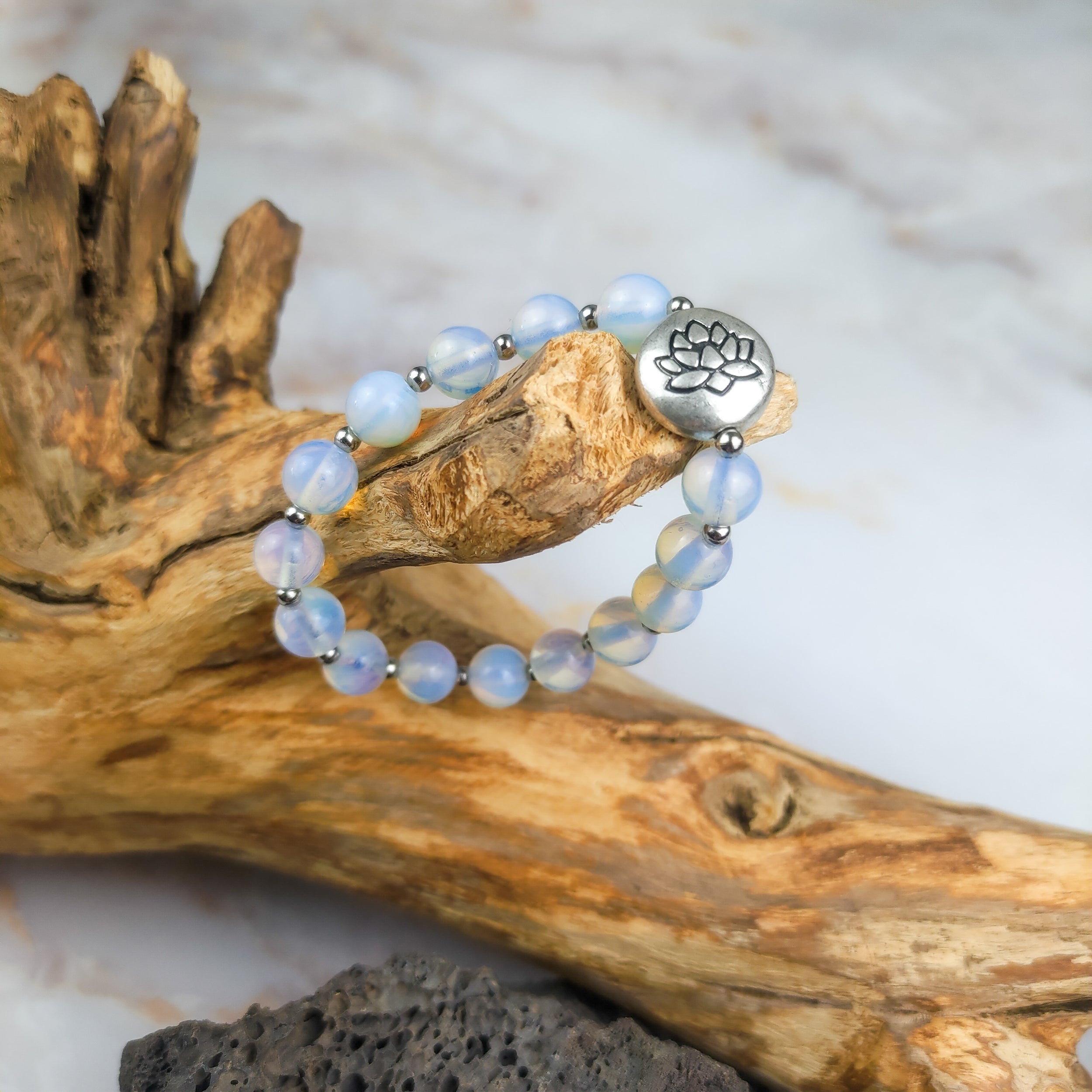 Bracciale loto opalite con perle traslucide e charm a forma di loto su fondo di legno