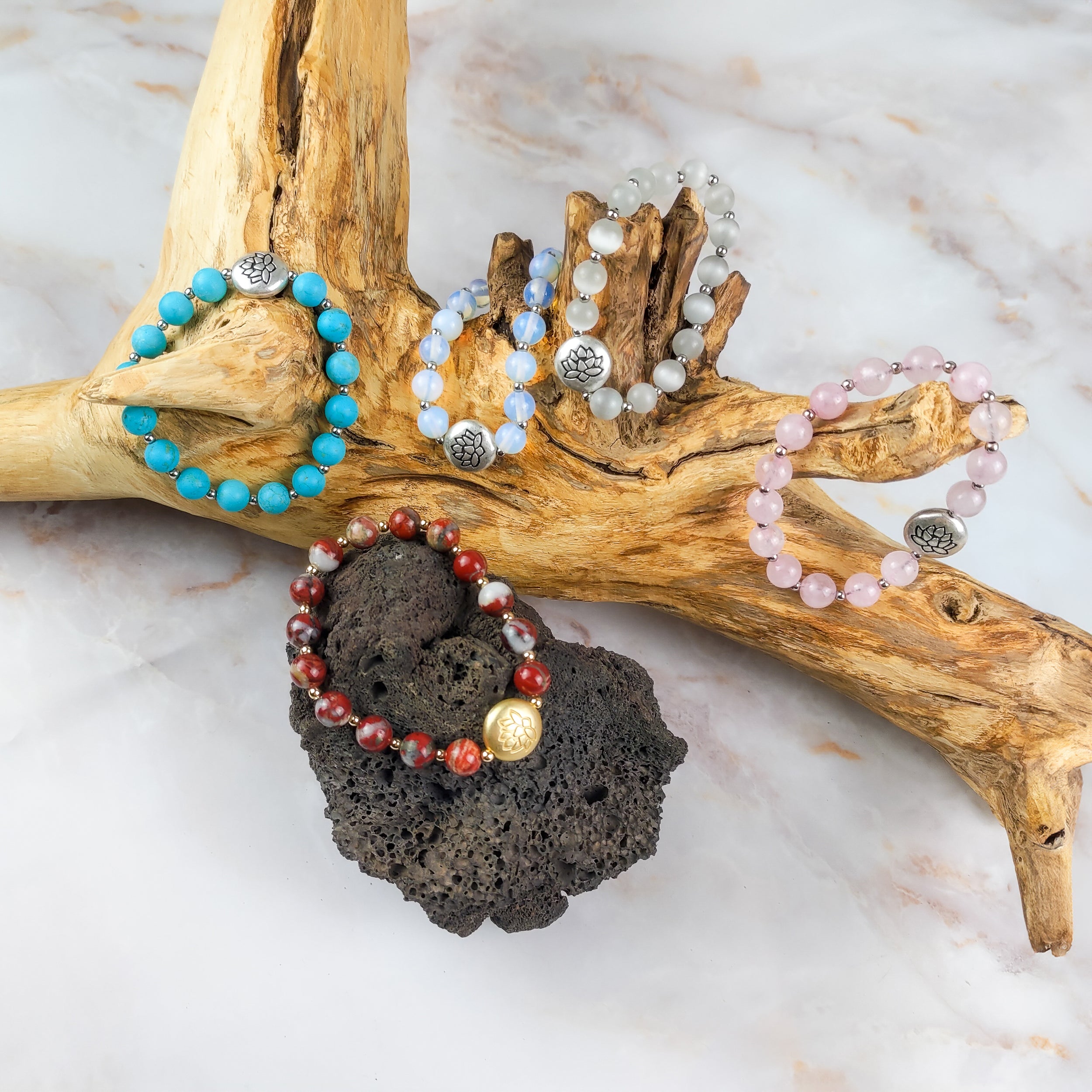 Bracciale loto turchese insieme a vari bracciali in cristallo su un tronco di legno artistico