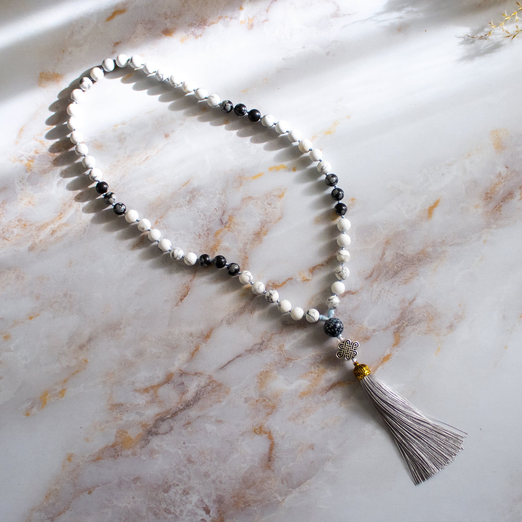 Collana mala ossidiana fiocco di neve con perline bianche e nere e nappo grigio