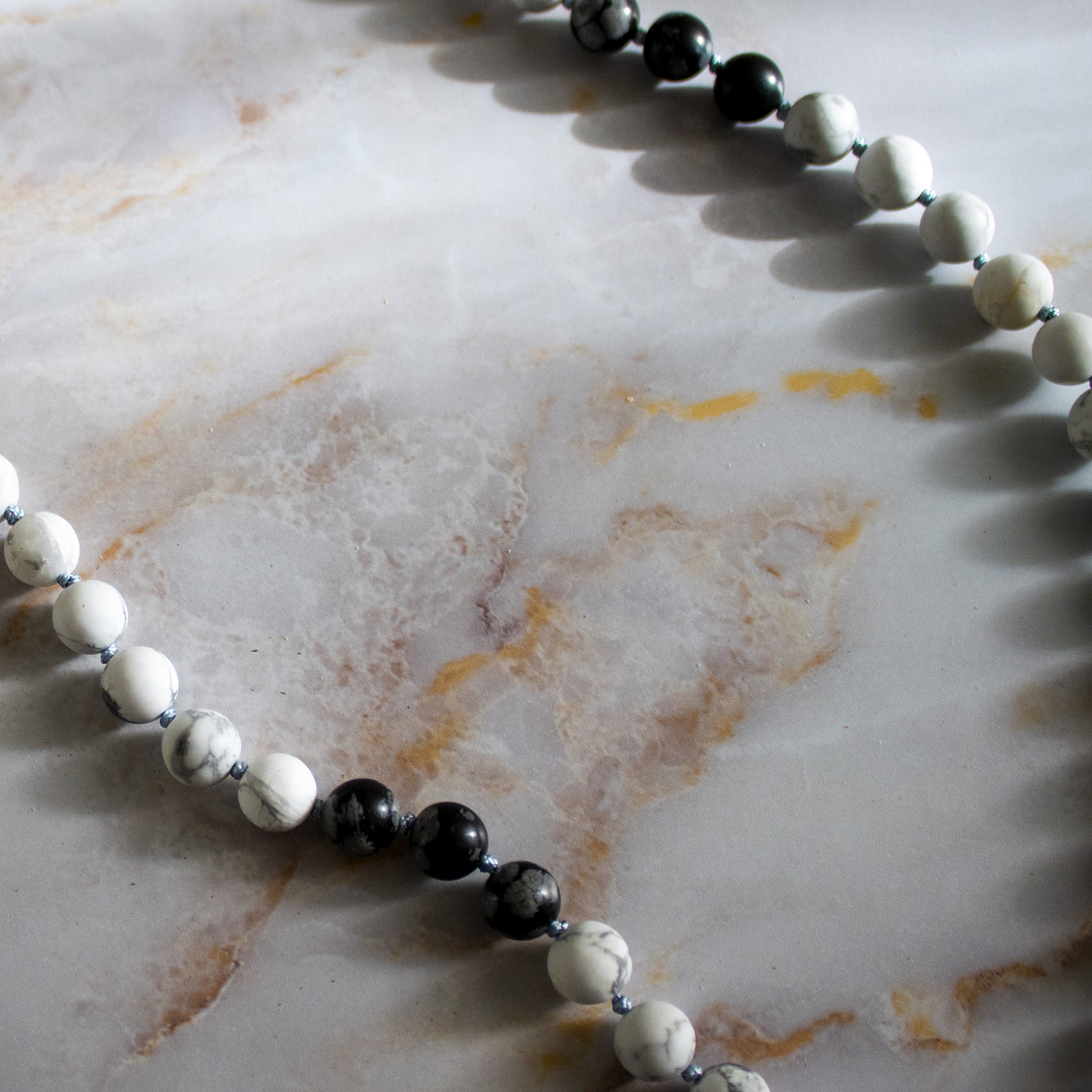 Collana in pietre di mala ossidiana fiocco di neve con perle bianche e nere su un tavolo elegante