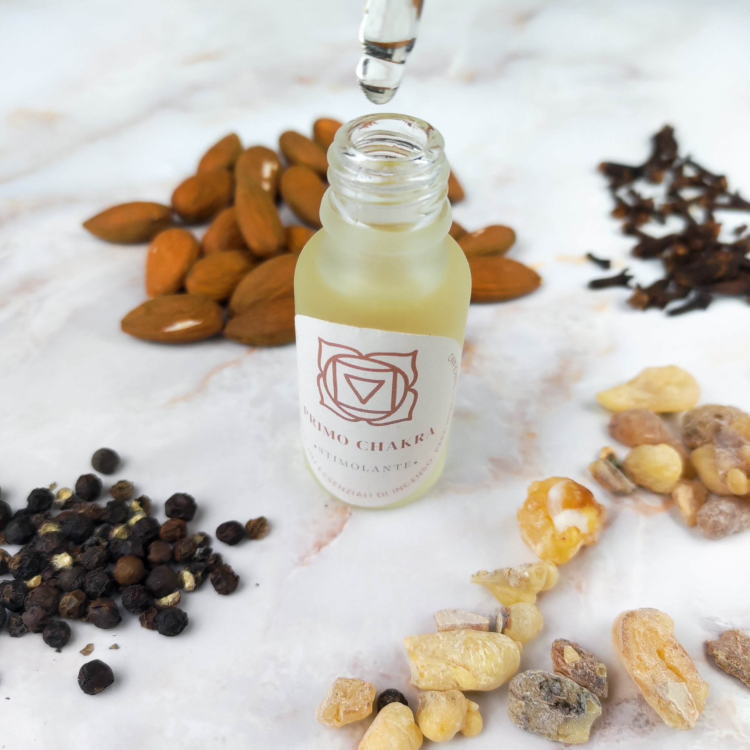 Olio per massaggi primo chakra in bottiglia con goccia e ingredienti naturali come mandorle e resina