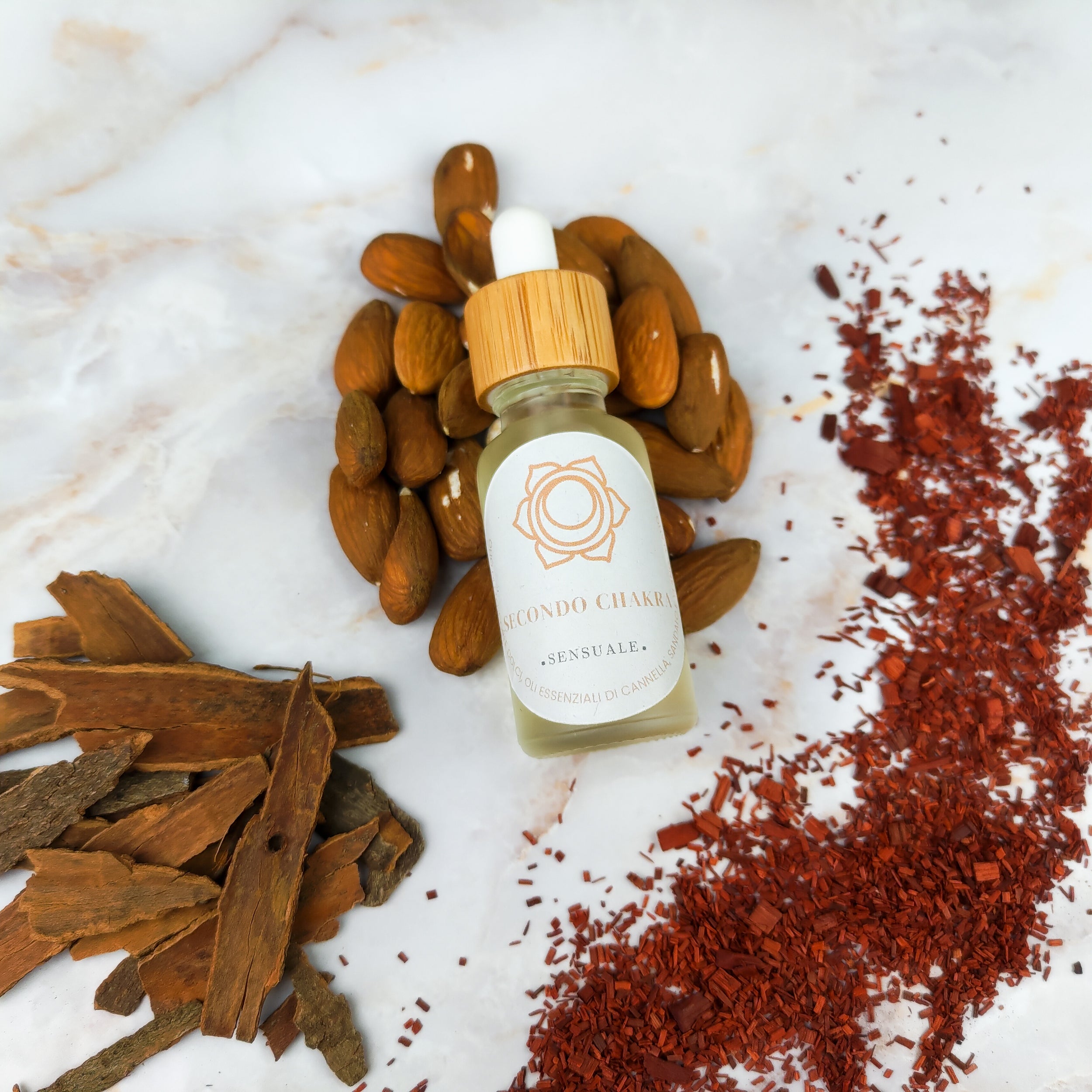 Olio per massaggi secondo chakra in bottiglia con pipetta, circondato da mandorle e spezie