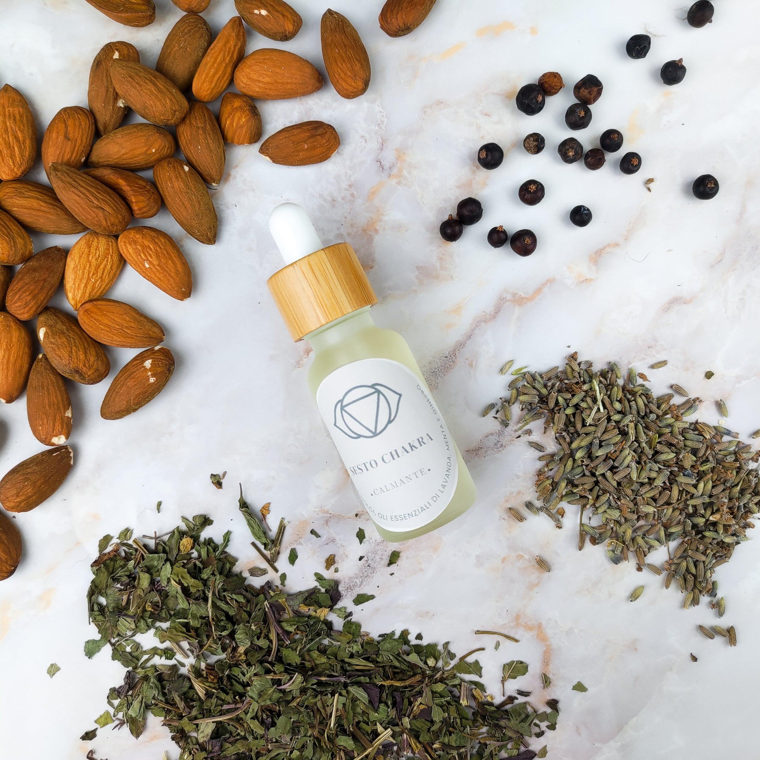 Olio per massaggi sesto chakra in bottiglia con tappo in legno, circondato da mandorle e erbe aromatiche