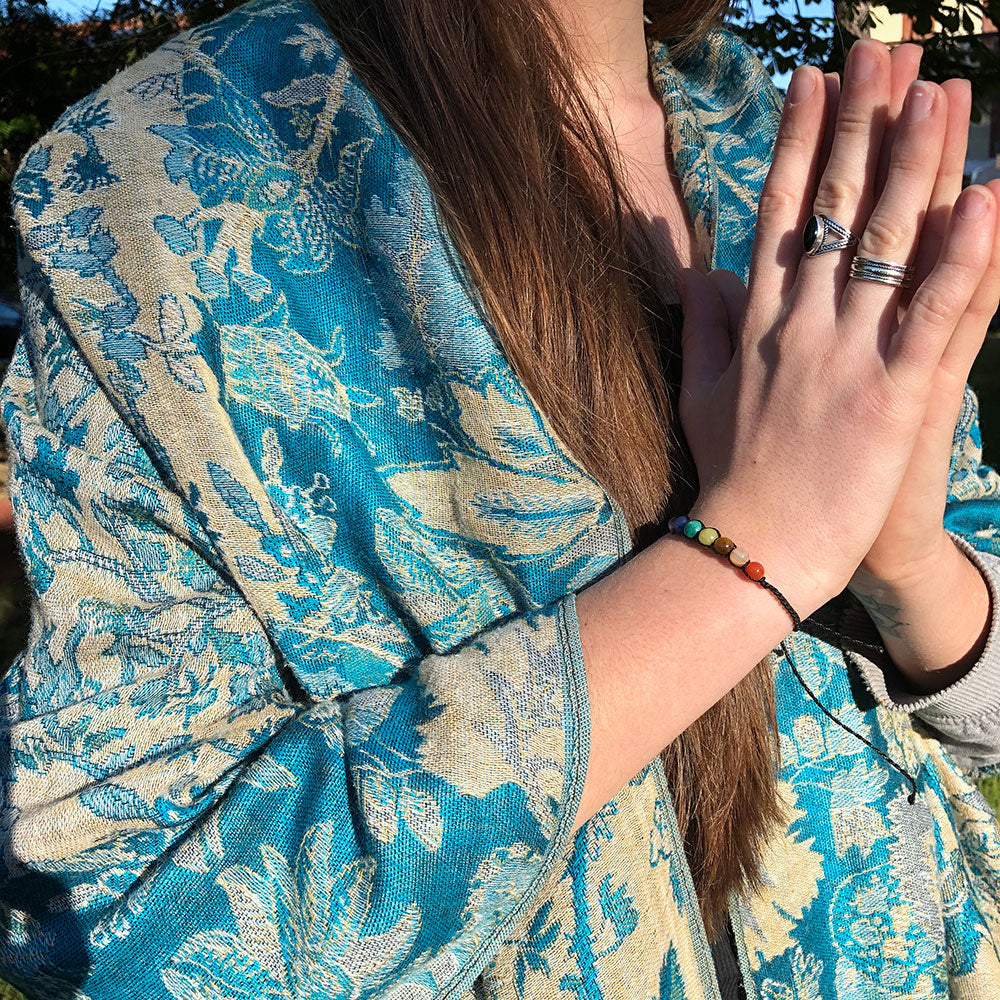 Bracciale chakra macramé indossato con mani unite in preghiera, design colorato e simbolico