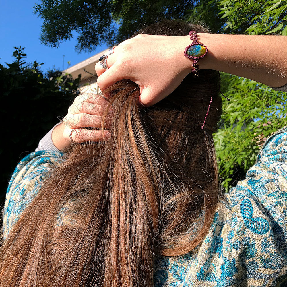 Bracciale macramé labradorite indossato su un polso con capelli lunghi in un ambiente naturale