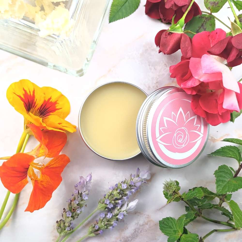Burro corpo naturale aromatico in contenitore aperto circondato da fiori colorati e foglie verdi