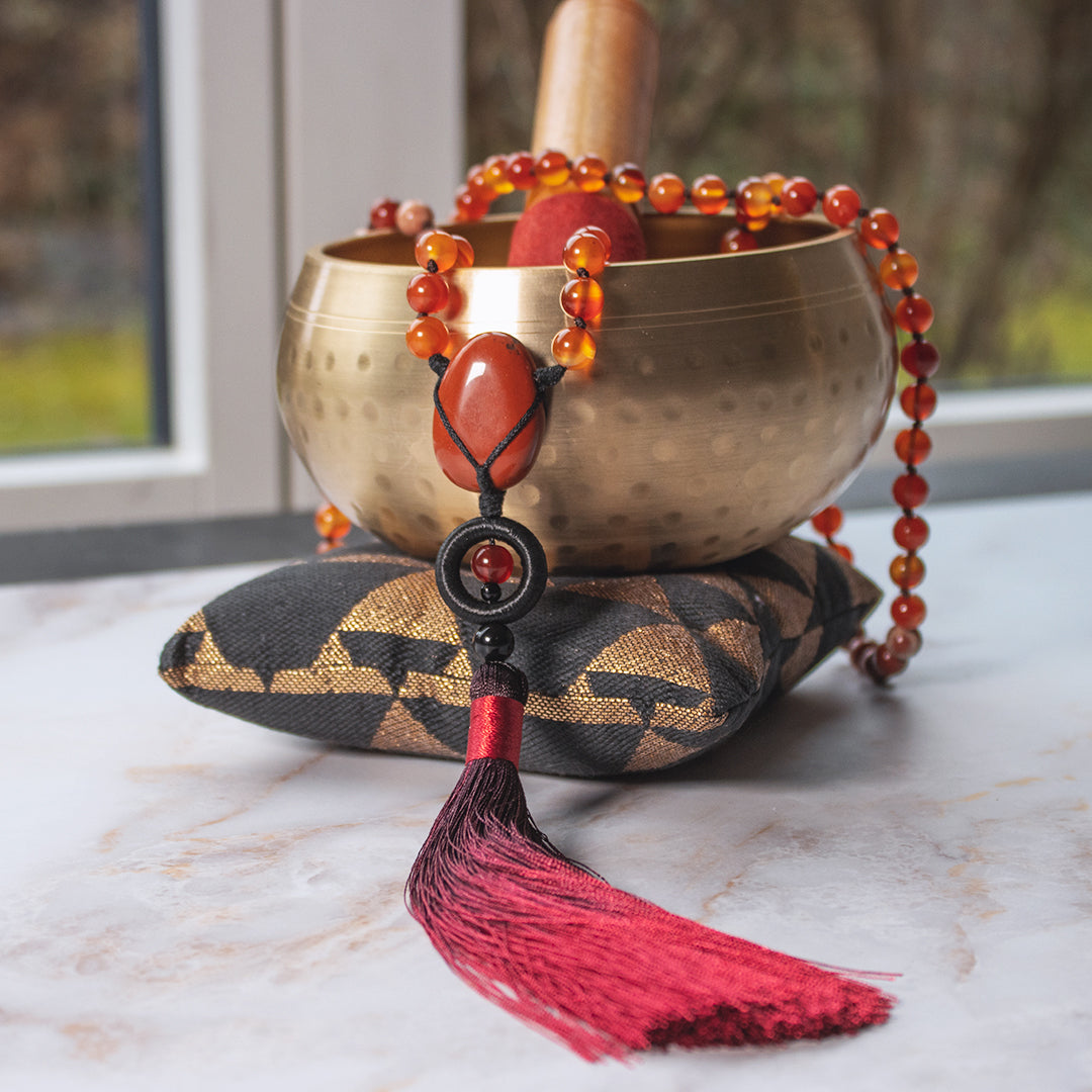Collana mala diaspro rosso e corniola con pom pom rosso e ciotola tibetana sullo sfondo