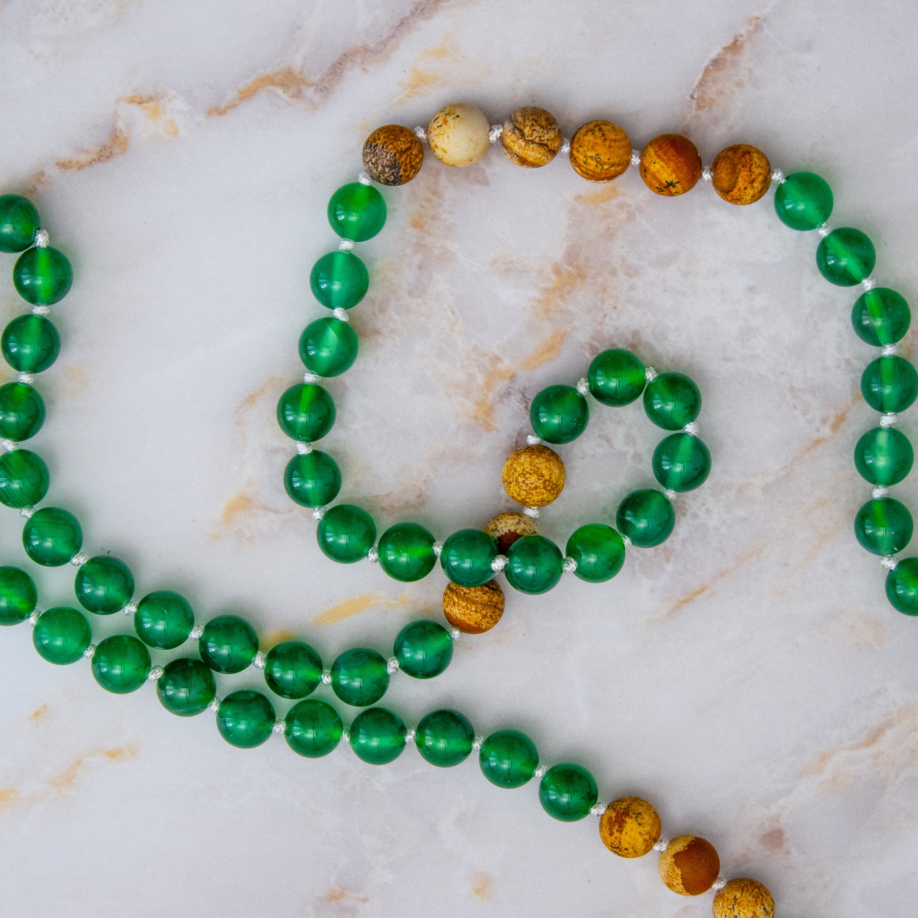 Collane mala diaspro verde onice con perle verdi e marroni su sfondo marmoreo
