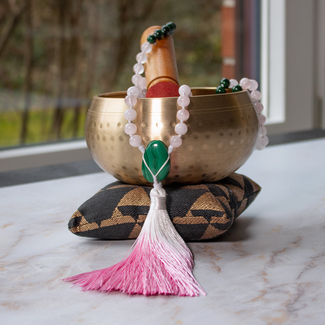 Collana mala malachite e quarzo rosa con frange, posizionata su un cuscino accanto a una ciotola tibetana
