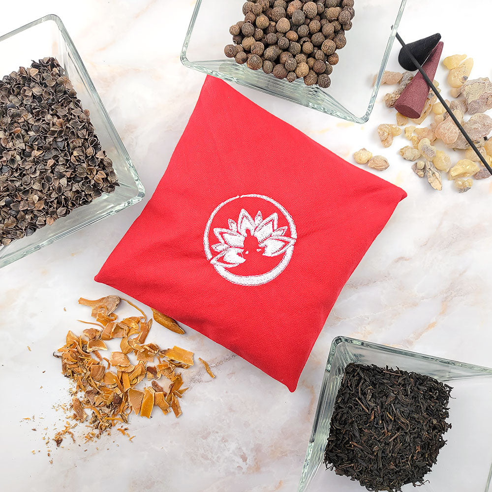 Cuscino rosso per profumatore ambiente primo chakra circondato da ingredienti naturali per aromaterapia