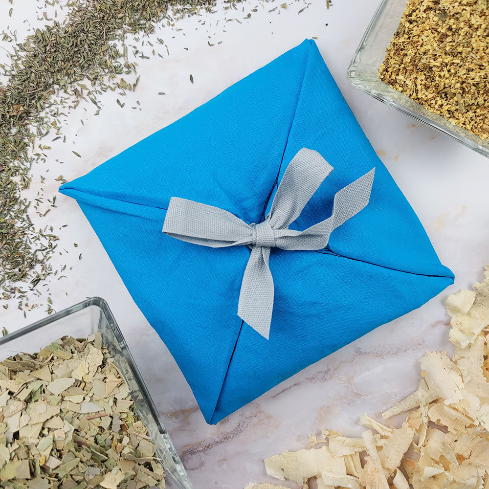 Profumatore ambiente quinto chakra avvolto in tessuto blu, circondato da erbe essiccate