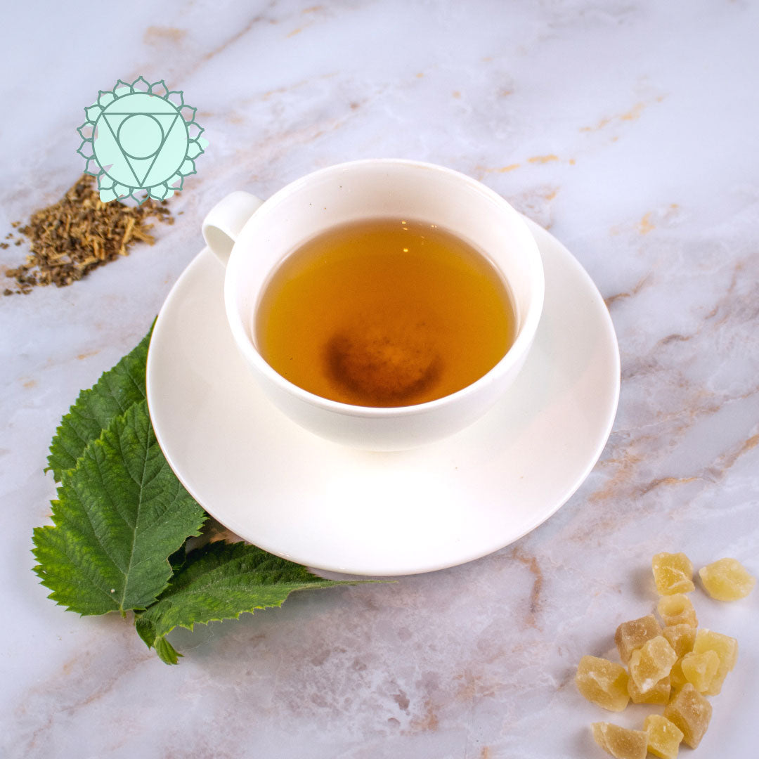Tisana quinto chakra in tazza bianca con foglie e radici circostanti sul piano marmorizzato