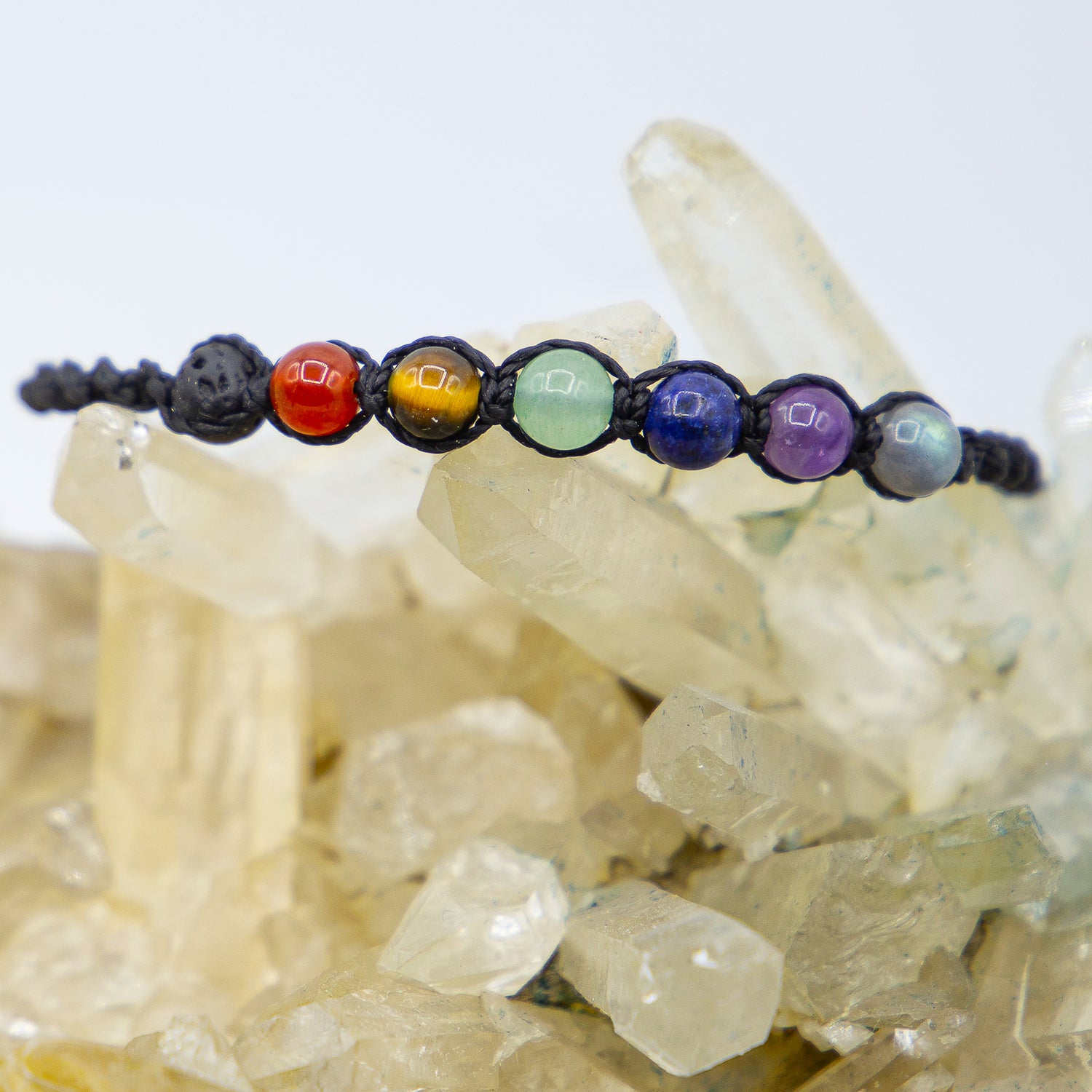 Bracciale chakra macramé con sfere colorate su fondo di cristalli trasparenti