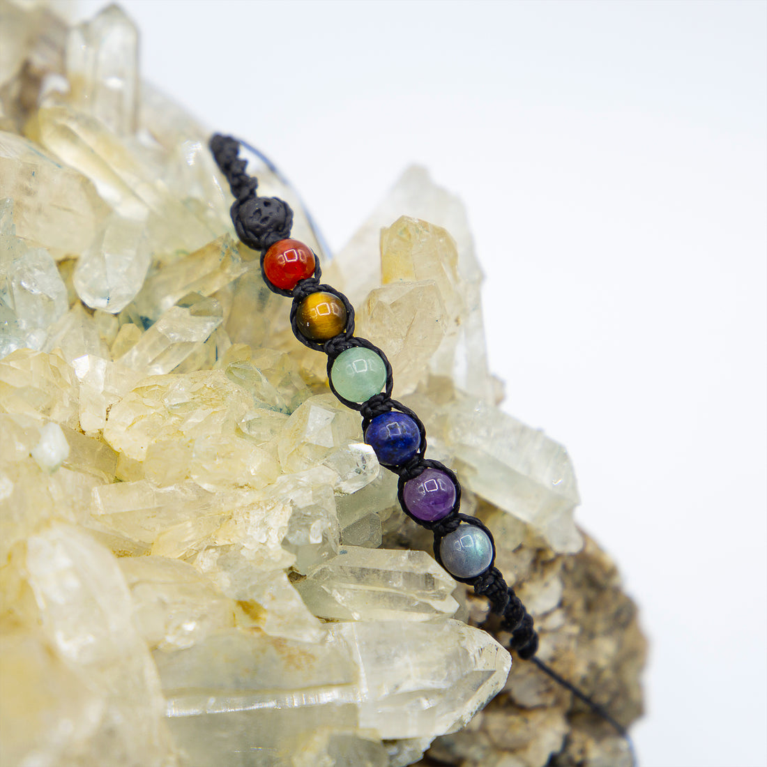 Bracciale chakra macramé con perline colorate su sfondo di cristalli trasparenti