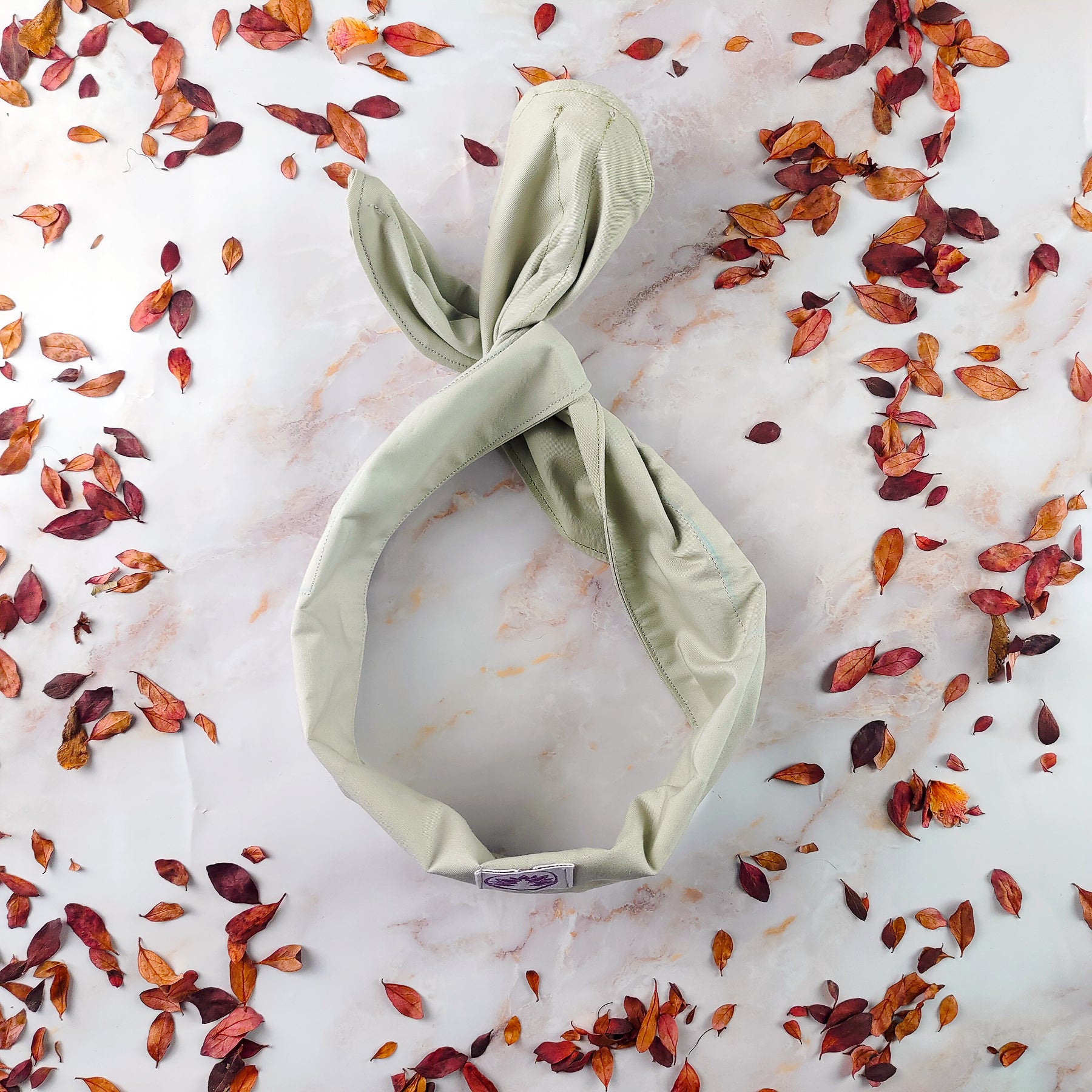 Fascia con ferretto artigianale di Shop Zen in tessuto beige su sfondo di foglie secche
