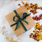 Confezione regalo box coccole invernali con nastro verde su sfondo di petali secchi