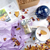 Confezioni regalo con box degustazione tisane, foglie secche e accessori da tè in un ambiente raffinato