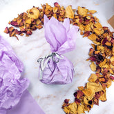 Confezione regalo raffinata con carta viola e petali di rosa, ideale per una box esperienza olfattiva.