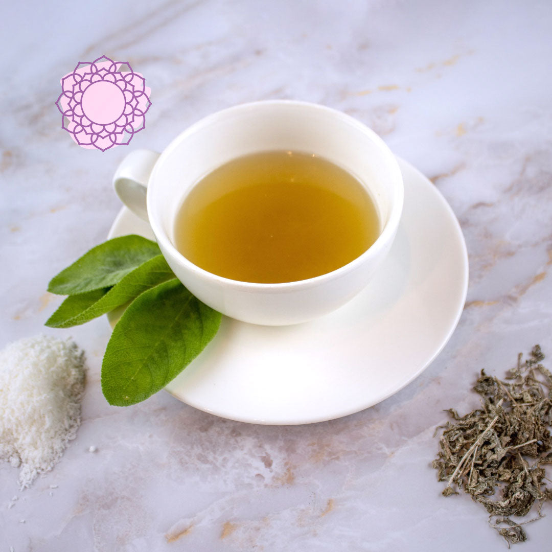 Tisana settimo chakra in tazza bianca con foglie verdi e ingredienti sul tavolo